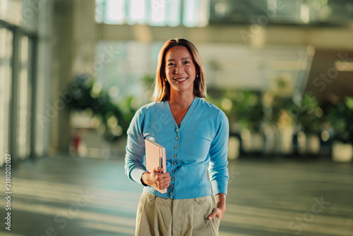 Photography Asian woman smiling, looking at camera, standing in office hallway, holding a no