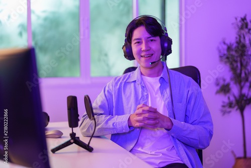 Obraz na płótnie Smiling Asian man wearing headset sitting at desk for video gaming stream