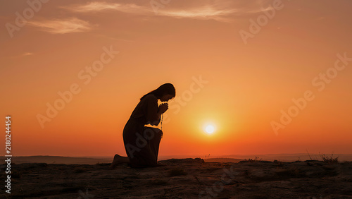 Faithful silhouette praying outdoors holding rosary cross at dusk