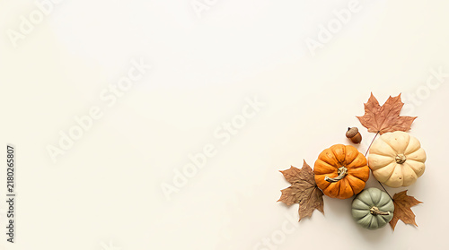 Small colorful pumpkins and dry autumn leaves arranged on a soft light surface