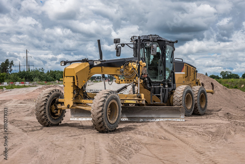 Fotografie Yellow motor grader levelling ground on road construction site.