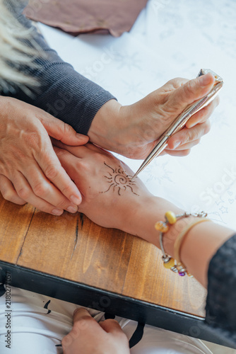 Konstfotografi Close-up of an artist applying a temporary henna-style sun design to a person’s
