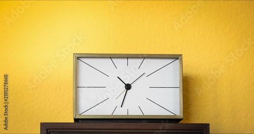 Time lapse of a retro vintage analog desk clock spinning fast against a vibrant yellow wall background