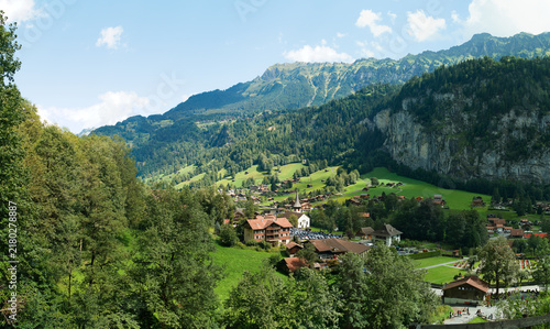 Panoramic View of Lauterbrunnen Village Surrounded by Lush Green Swiss Alps Mountains and Traditional Houses Under Blue Sky