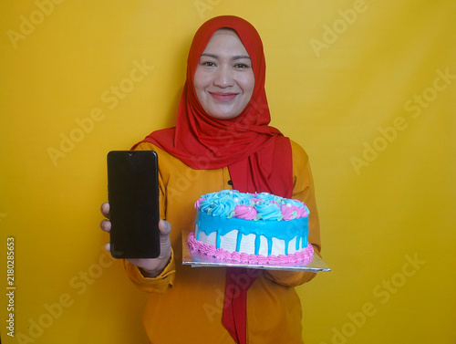 Smiling Young Asian Muslim Woman Showing Blank Screen Phone For Mock Up While Holding A Birthday Cake