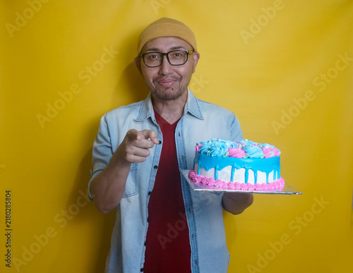 Young Asian Man With Beanie Hat And Glasses Pointing At Camera Showing It's You Gesture While Holding Tart Cake