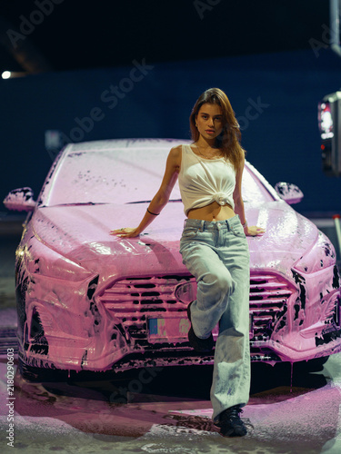 Young Woman Leaning On Hood Of Car Covered In Pink Foam At Night Self Service Wash Station