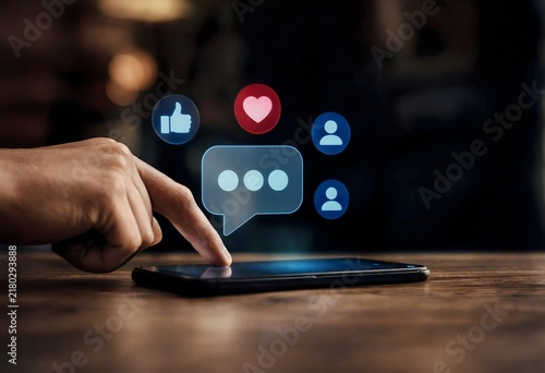 Social Media Interaction: A finger hovers over a smartphone screen displaying social media icons like a chat bubble, like, heart, and profile silhouette.