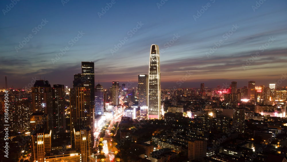Obraz premium Twilight Cityscape With Tall Modern Skyscraper And Illuminated Buildings