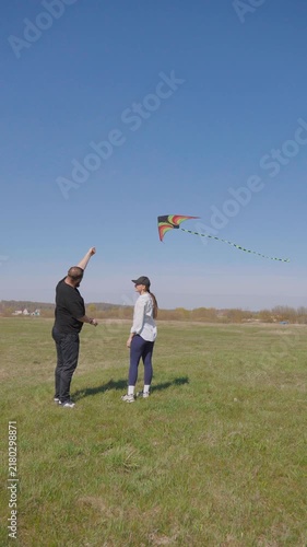 Young couple having fun together on a sunny day in nature, with the woman running and launching a colorful kite into the blue sky while the man watches and cheers her on