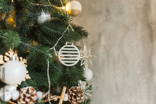 Close up of decorated Christmas tree with laser cut wooden ornaments pine cones and glowing fairy lights.