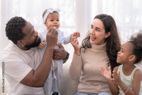 A fun-loving father with his baby holds up his giggling baby to play in a bright home living room, full of fatherhood joy and play captured in soft natural light.