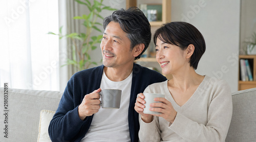 Plakat ソファでマグカップを手に微笑みながら未来を想うミドル世代の男女