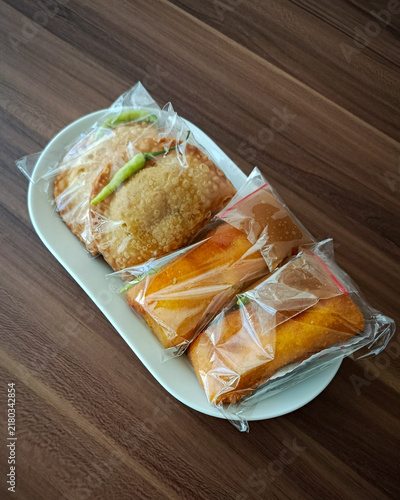 Top view of traditional Indonesian fried snacks pastel and risoles wrapped in clear plastic on a white plate.