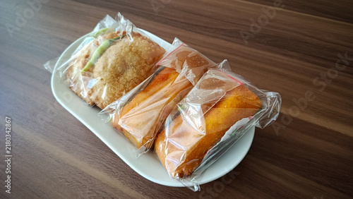 Top view of traditional Indonesian fried snacks pastel and risoles wrapped in clear plastic on a white plate.