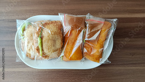 Top view of traditional Indonesian fried snacks pastel and risoles wrapped in clear plastic on a white plate.