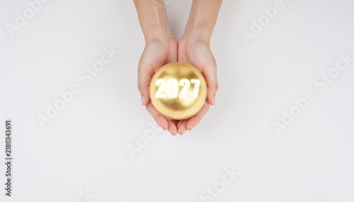 Hands holding a golden sphere with the number 2027.