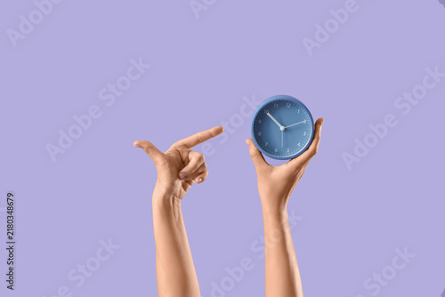 Konstfotografi Female hands pointing at alarm clock on lilac background