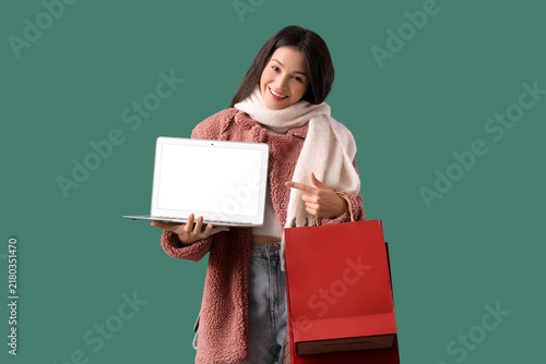 Beautiful young woman in warm clothes with shopping bags pointing at modern l...