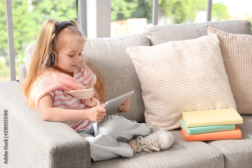 Cute little girl in headphones listening to audiobook with modern tablet comp...