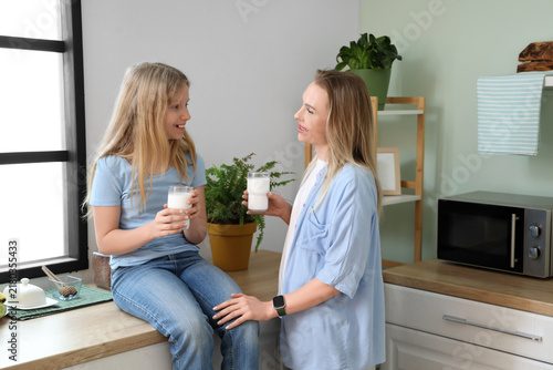 Happy daughter and her mother with cups of milk sitting in kitchen