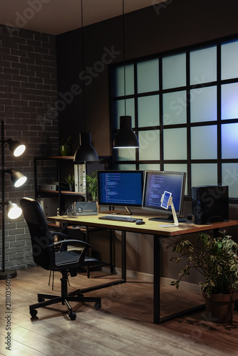 Interior of dark office with programmers workplace and shelf unit at night
