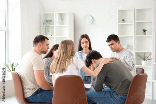Young people calming upset man at group therapy session