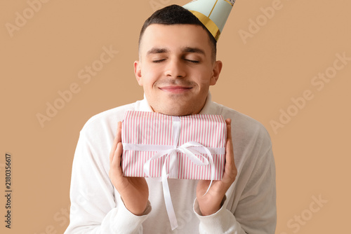 Fotografie Young man in party hat with gift box celebrating Birthday on brown background
