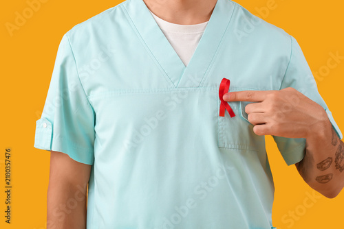 Male doctor with red ribbon on yellow background, closeup. World AIDS day con...