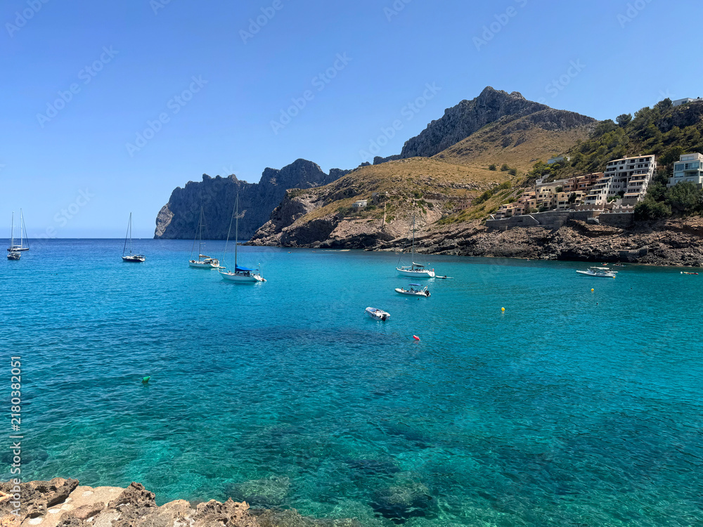 Obraz premium View over Cala Sant Vicenç, in the municipality of Pollença, on the island of Mallorca, Balearic Islands, Spain, showing small boats anchored in the turquoise bay beneath a rocky headland.