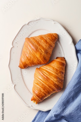 Freshly baked croissants on a decorated beige plate with a blue tea towel. Top view