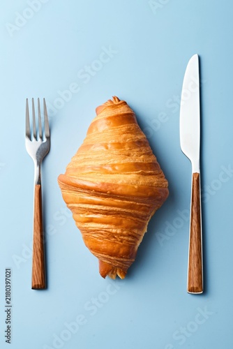 Croissant with a fork and knife on a blue background. Top view