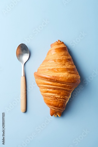 Croissant with a tea spoon on a blue background. Top view