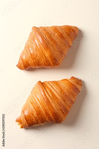 Fresh croissants laying on a flat beige surface. Top view