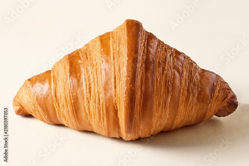 Fresh croissant laying on a flat beige surface viewed from the side