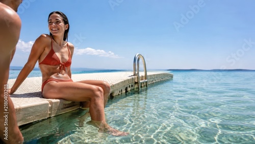 A couple enjoys a peaceful moment by the shimmering water at a beautiful sunny spot, surrounded by a clear blue sky and a tranquil sea on a warm summer day