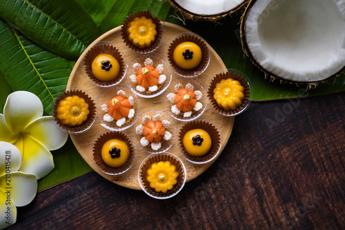 Traditional golden Thai sweets are placed on a wooden table, adorned with banana leaves and flowers