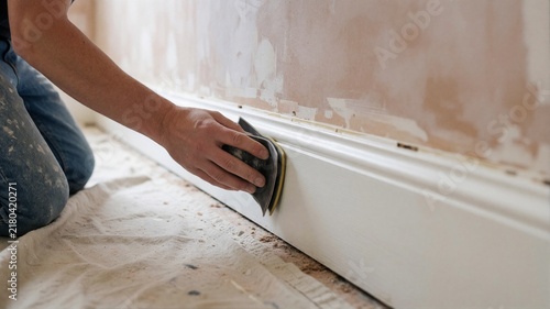 Worker sanding white baseboard during home renovation