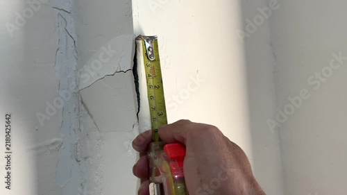 Measuring crack size on damaged wall corner with tape measure
