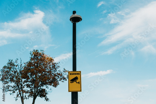Foto A surveillance camera and warning sign stand on a pole against a blue sky