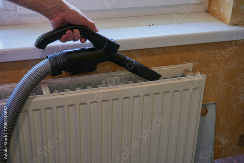 Cleaning home heating radiator with vacuum cleaner, Person cleaning inside of modern heating radiator with vacuum nozzle close up
