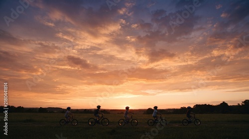 Sunset cyclists riding through open field under dramatic sky glow
