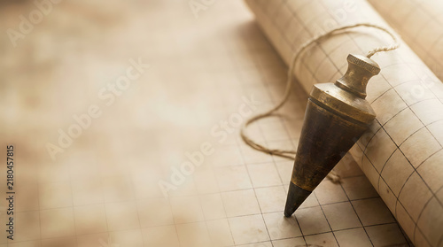 Vintage Brass Plumb Bob Tool Resting on Gridded Architectural Blueprint Paper for Precise Construction Measurement and Engineering Design