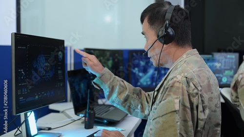 Senior military officer in camouflage uniform uses a computer and headset to analyze cyber intelligence and surveillance data