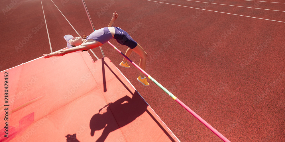 Obraz premium Teenage athlete clears high jump bar in overhead stadium view. Concept of youth sport, flight technique, agility, competition, achievement and athletic development.