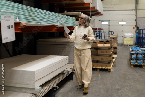 Woman reading a shopping list and using a smartphone in a hardware store