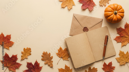 Autumn flat lay with open blank notebook, envelope, pumpkin and dry leaves on beige background