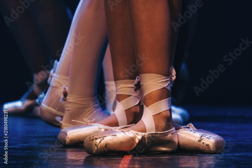 Фотография Dancers' feet in worn pointe shoes, standing ready on a dark stage, conveying de