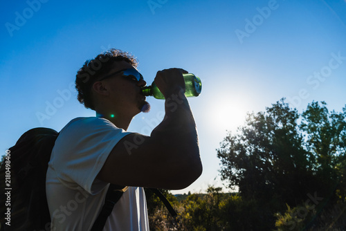 Принти на полотні Hiker with backpack drinking water from a bottle, silhouetted against a bright b
