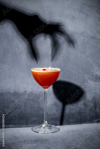 Halloween cocktail on dark background. Drink in coupe glass with witch hand shadow. Creative party food and beverage. Spooky, scary, fun, bewitched, horror. Bar holiday menu. Vertical, selective focus